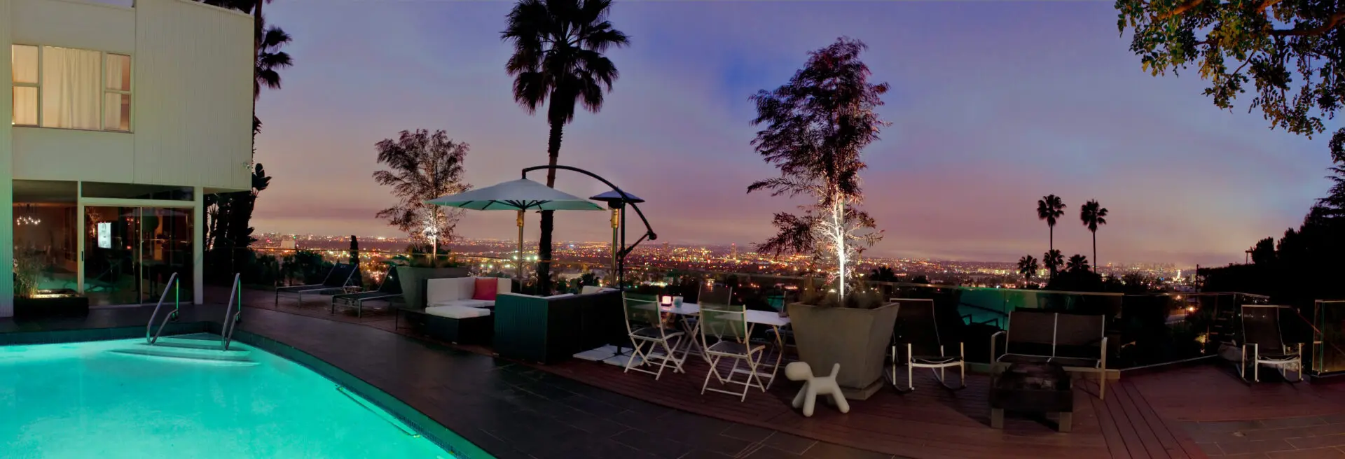 A patio with tables and chairs, umbrella and palm trees.